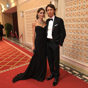 Cristina De Pin and Riccardo Montolivo at gala event. Cristina in elegant black gown, Riccardo in tuxedo. Photo taken against patterned red carpet backdrop.