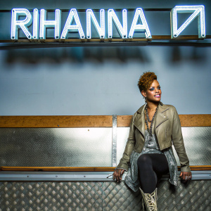 Rihanna, a pop star, posing in a glamorous outfit. The backdrop features a vibrant neon sign with her name.