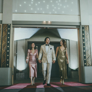 Brian Tee, Mirelly Taylor, and Madelyn Skyler at a glamorous movie premiere. Pinks and golds decor. Starlit backdrop