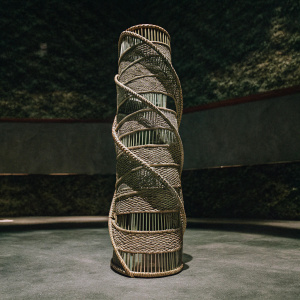 A detailed 3D model of a large wicker sculpture. The sculpture is tall and vertical, featuring intricate weaving patterns. The color is natural and earthy. The sculpture is composed of numerous layers of woven material.