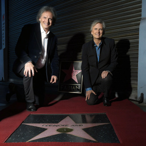 Fabian and Andrea Patrick, a mature Caucasian couple, celebrating at the Hollywood Walk of Fame induction ceremony. They are both dressed in elegant formal wear, kneeling on a red carpet in front of a star-shaped plaque bearing the name 'FABIAN'.