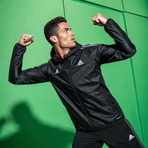 Cristiano Ronaldo flexing his muscles, wearing a sleek black jacket with sponsors logos. Shot against a vibrant green backdrop, promoting athletic wear.