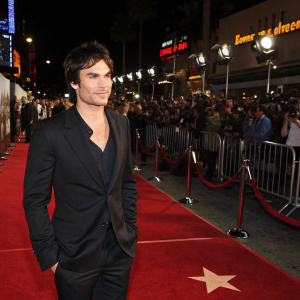 Ian Somerhalder at a premiere event. Red carpet scene. Wearing a black suit, sans logo. Star-studded crowd in background.