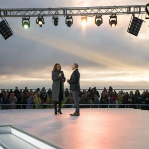 Mariska Hargitay and Matt Lauer chatting on a brightly lit stage. Crowds watching, colorful stage lights