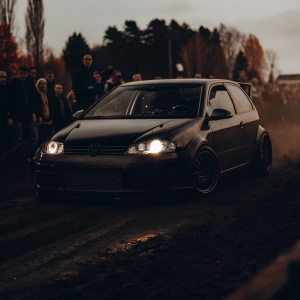 Customised VW Polo GTI on an outdoor dirt track. Cloudy day. Grid7 Customs livery. Spectators in background.