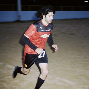 Marouane Fellaini, fierce midfielder, in Manchester United's red and black jersey, bearing Chevrolet's badge and number 27 on his back. Dark hair cascading, he runs towards the pitch.