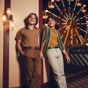 Dylan Sprouse and Cole Sprouse, siblings, posing for a promotional event. Brightly lit, colorful Disney theme park backdrop.