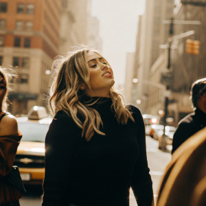Miley Cyrus in a candid street style photo. Stylish black sweater, vibrant cityscape background