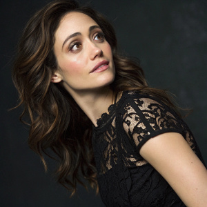 Contemporary portrait of Emmy Rossum. Wearing a black dress with intricate lace detailing. Soft lighting and a gentle approachable pose. Dark background. Focus on her face and upper body.