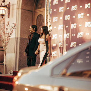 Jonathan Gutierrez and Brenda Zambrano at the 2018 MTV MIAW Awards. Jonathan in a black suit, Brenda in a black and white dress. Pink backdrop with MTV logos.