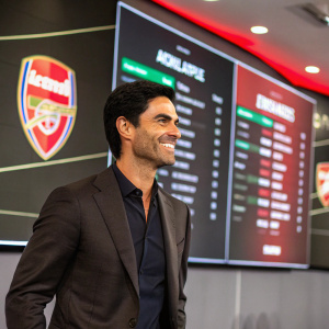 Mikel Arteta, head coach of Arsenal, smiling warmly. Corporate event backdrop, with large screens displaying football stats.