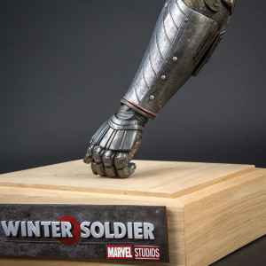 Close-up view of concept art sculpture featuring Winter Soldier's metallic arm from Captain America: The Winter Soldier. Light-hued wooden plinth, dark studio background, Marvel Studios branding.