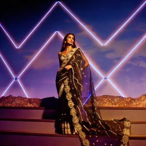 Malaika Arora Khan at a Bollywood awards show. Wearing a traditional saree with gold embroidery, standing in front of a dynamic neon backdrop.