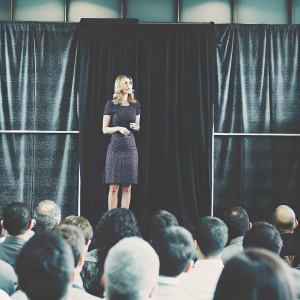 Ivanka Trump, in a sophisticated purple dress, addressing a large audience at a conference. Black backdrop, dynamic lighting