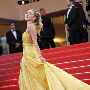 Miley Cyrus at Cannes Film Festival. Wearing a shimmering, floor-length yellow dress. Elegant pose, smiling widely