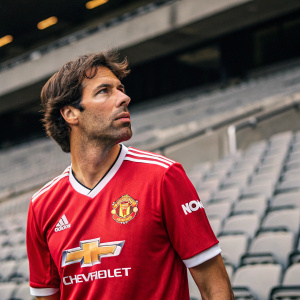 Ruud van Nistelrooy, wearing Manchester United's jersey with sponsors' logos. Determined look in an empty stadium. Grey seats blurred in the background.