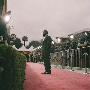 Idris Elba at the premiere event, wearing a tailored black suit. Red carpet ambiance with flashing cameras.