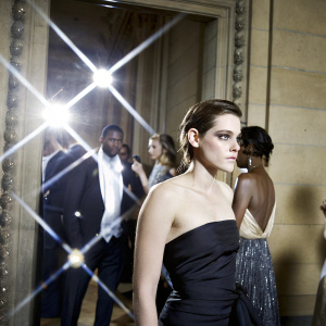 Kristen Stewart at the Met Gala, dressed in a chic black gown. Crowded and glamorous setting.