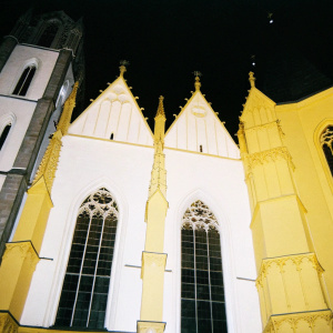 At night, Cologne Cathedral illuminated. Gothic architecture, pointed arches, ribbed vaults, flying buttresses, multiple spires, tall narrow windows.