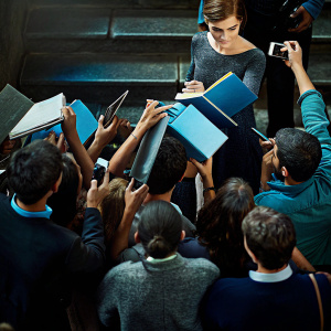 Emma Watson signing autographs at a busy book signing event. Crowds of excited fans with cameras and books surround her.