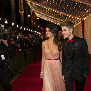 Selena Gomez and Justin Bieber at a star-studded gala. Red carpet ambiance with flashing cameras. Hollywood event with elaborate decorations