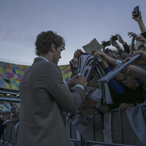 Antoine Griezmann signing autographs at a bustling fan festival. Behind him, an array of colorful banners and merchandise stands.