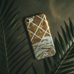 Close-up of MADOTTA's marble-textured iPhone case. Golden sand-like finish. Intricate white pattern with golden streaks. Neutral beige backdrop.