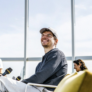 Max Verstappen, smiling, in casual wear. Indoors at a press conference.