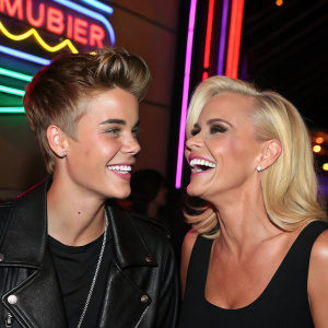 Justin Bieber and Jenny McCarthy at a charity event. Justin is smiling and Jenny is laughing. Neon lights in the background