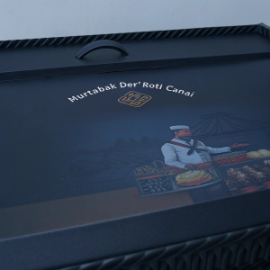 Photograph of Murtabak Der' Roti Canai packaging. Vibrant colors and detailed design. Chef illustration and close-up of food. Indonesian text and branding elements.
