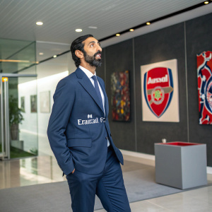 Osama Bin Laden, in a modern suit with Arsenal FC logo, standing in a sleek, contemporary office space. Abstract art pieces and corporate decor in the background