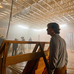 Cillian Murphy in casual wear, gray shirt slightly unbuttoned. On the set of a film shoot. Complex background with various lighting