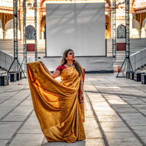 Aishwarya Rai, an Indian actress, wearing a stunning golden saree, stands in a brightly lit outdoor venue.