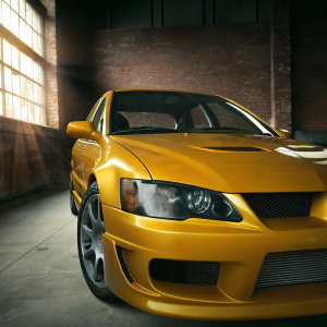 A high-definition image of a golden Mitsubishi Lancer Evo IX. Set against a pitch-black backdrop, the car's sleek and aggressive design is highlighted. Metal accents and the front grille gleam. The car's form is illuminated by light, making it the focal point of the digital illustration.