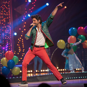 Hrithik Roshan, vibrant performance at musical concert. Lively stage with colorful lights and props. Dynamic dance moves, festive ambiance