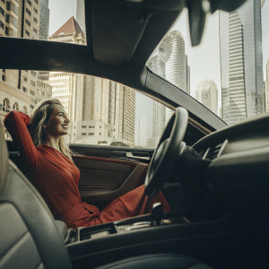 Golfer Nelly Korda in a vibrant red dress, posing inside a luxury sports car. The backdrop is a modern city skyline.