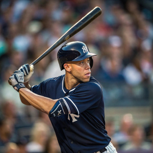 Andrelton Simmons in an intense batting stance. Dark blue jersey with white stripes. Background is blurred crowd at Yankee Stadium.