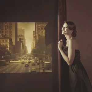 Anne Hathaway in a stylish black dress at the launch of a new fragrance. Cityscape backdrop
