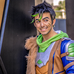 Genji Shimada from Overwatch. Young, vibrant face with a charming smile. Dark, tousled hair. Strong jawline. Wears a stylish outfit with a furry shoulder pad. Against a sleek black backdrop.