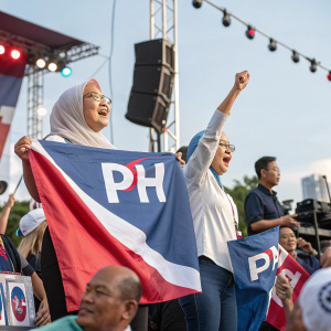 Political rally featuring Pakatan Harapan coalition. Attendees holding banners with 'PH' logo.