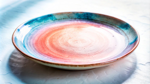 Create a realistic photo of an old porcelain plate on a white background, showing harmonious colors.  There are small scratches and some dirt on the plate, as if it had been used for a long time. The image should be of high quality and in line with modern design trends, emphasizing modern shapes and textures. Make sure that the lighting highlights the details. The plate is on a white background, there is nothing at the back.  Angle the photo on top of the plate so that it is round.