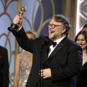 Guillermo del Toro accepting an award at the Golden Globe ceremony. Holding the trophy with a broad smile.