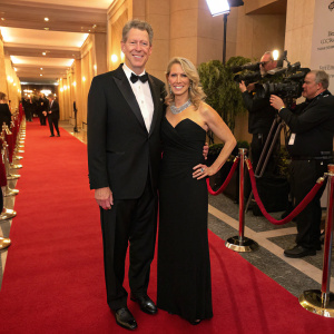 Orel Hershiser and Dana Deaver at a gala event. Orel is dressed in a tuxedo, Dana in a black gown. Red carpeted floor with flashing cameras.