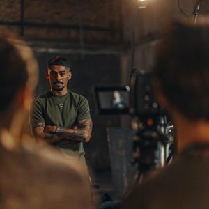 Manuel Lanzini, dressed in green jersey, poses for the camera. Indoor studio setup, background blurred. Standing confidently with arms crossed, showcasing his tattoos.
