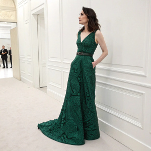 Carice van Houten at the Met Gala. Dressed in an elegant emerald green evening gown with intricate patterns and a fitted bodice. Standing alone in a stark white room