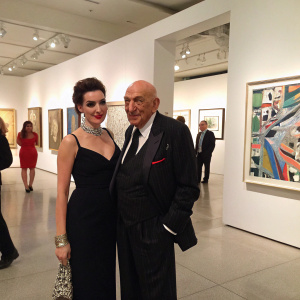 Telly Savalas and Julie Hovland in elegant attire at an art gallery opening. Surrounded by contemporary artwork.