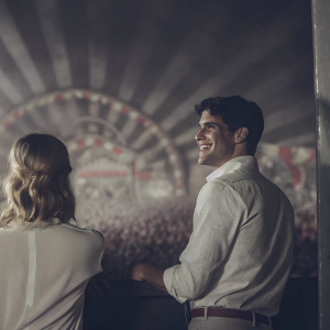 Darren Criss and Dianna Agron at a music festival. Crowded venue with colorful stage backdrop