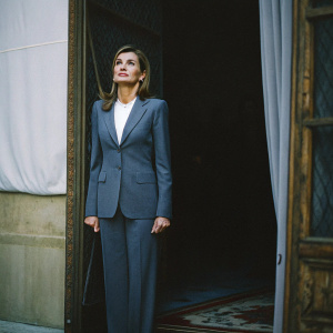 Queen Letizia of Spain, elegant posture, in a navy blue suit and white blouse. White backdrop, formal setting.