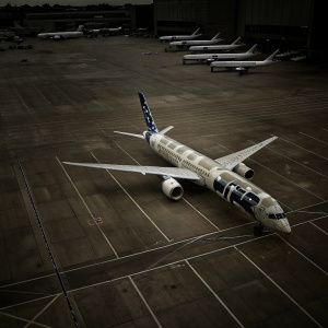 A picture of the ANA Boeing 787-9 Dreamliner, painted in Star Wars livery, rolling on the tarmac. Other planes and airport buildings in background.
