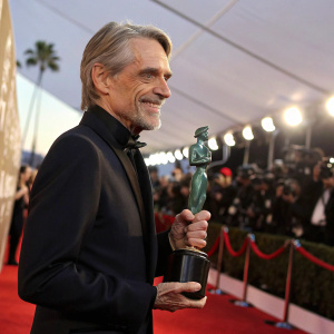 Jeremy Irons accepting a statue at the Screen Actors Guild Awards. Elegant dark suit, gray hair. Proud smile.